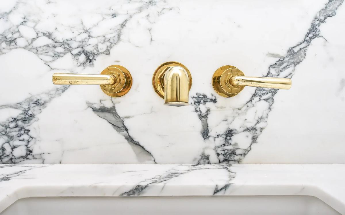 Unlacquered brass wall-mounted faucet against veined marble