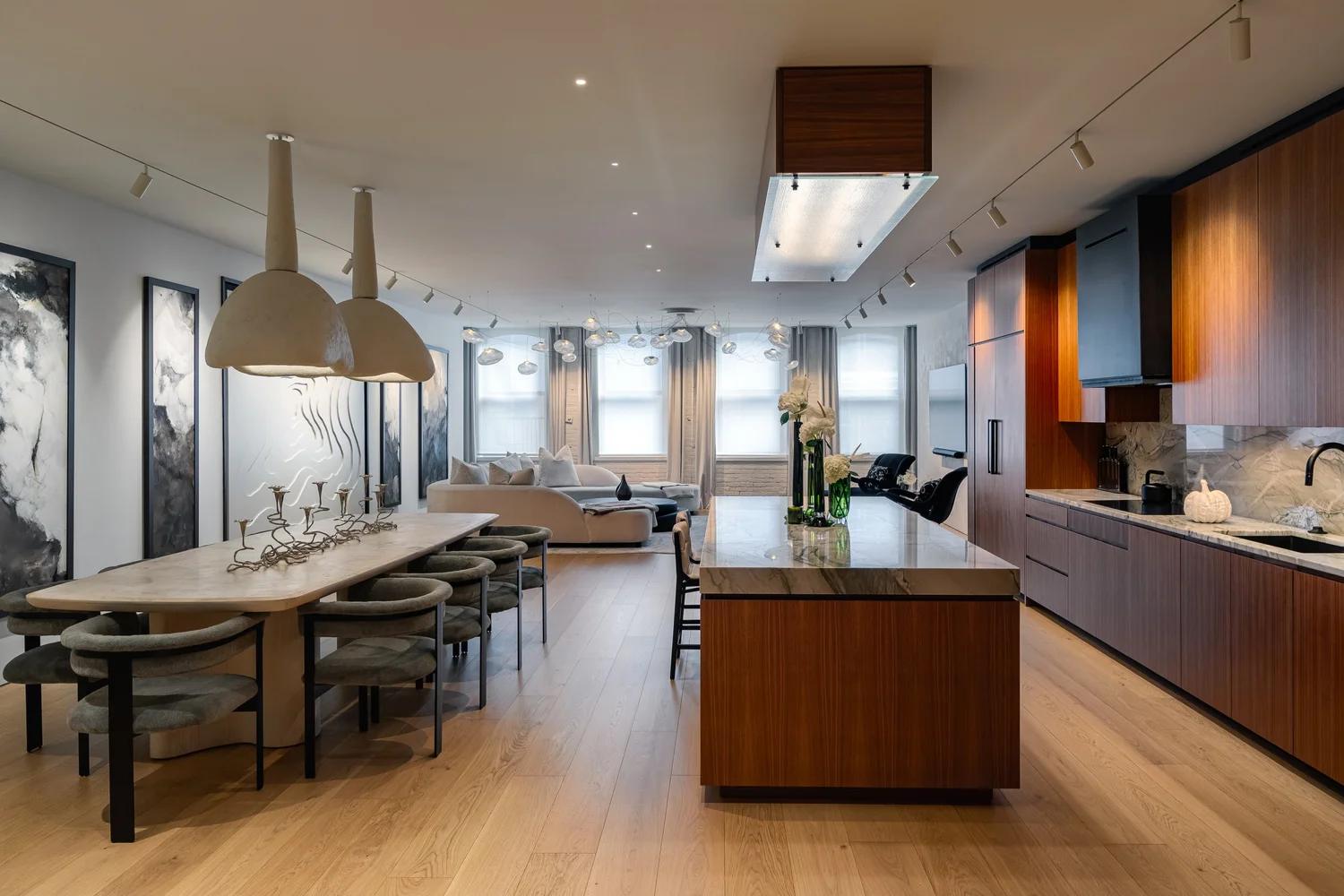 Open-plan kitchen, dining and living room in white with a woven-stool island, coffered ceiling and capiz chandelier, looking out to the water